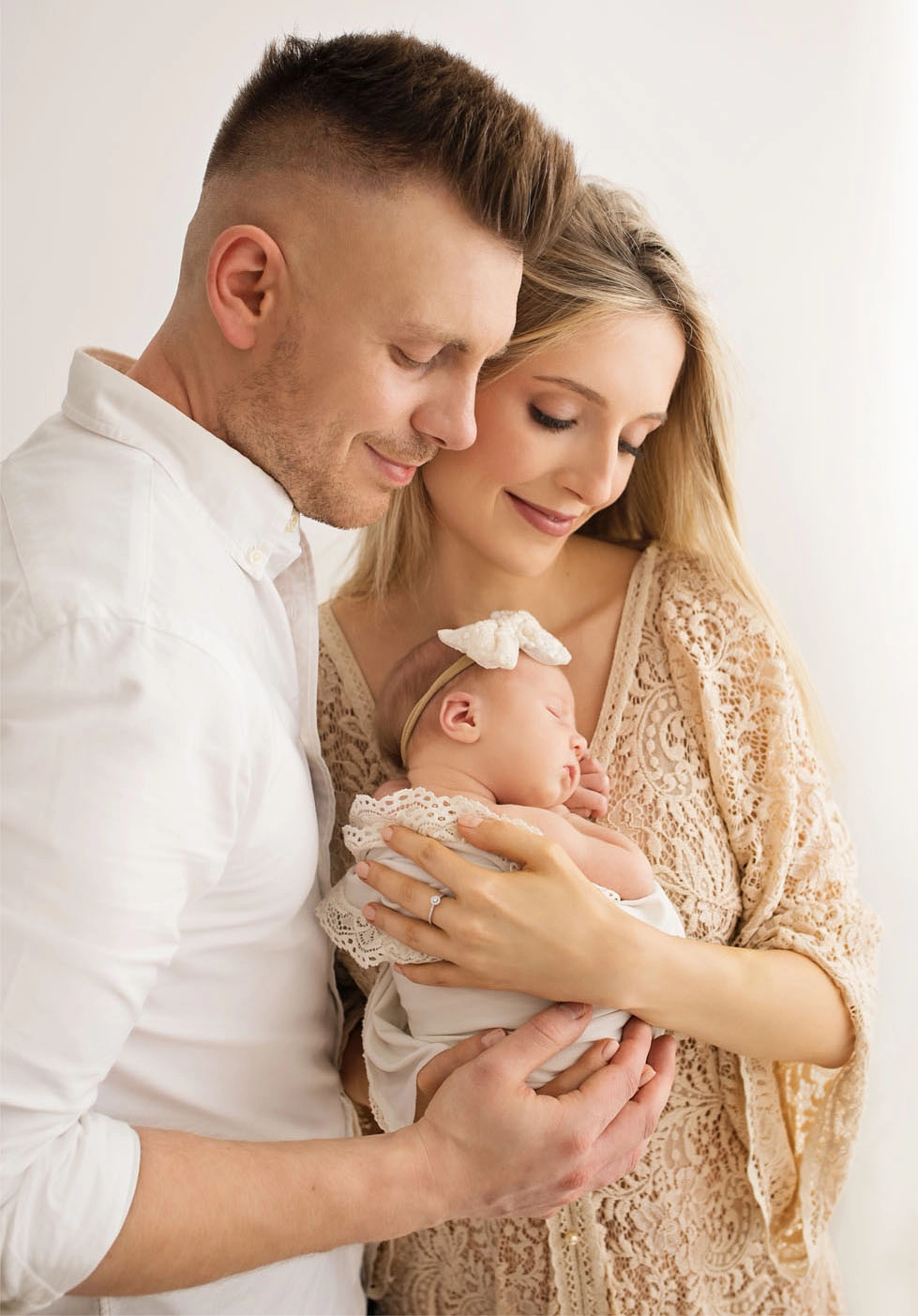 Parents cuddling their sleeping newborn with a bow during a newborn session in a bright studio in Warsaw