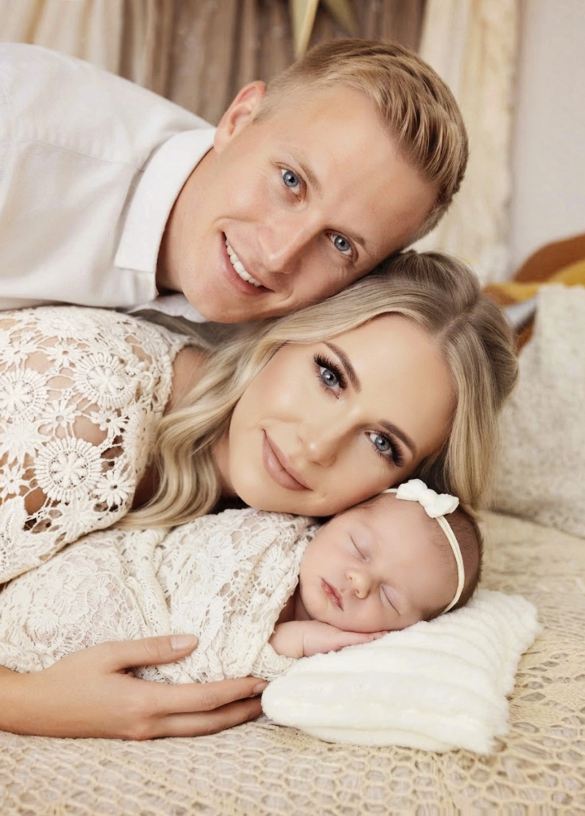 Smiling parents cuddling their sleeping newborn with a bow during a studio session